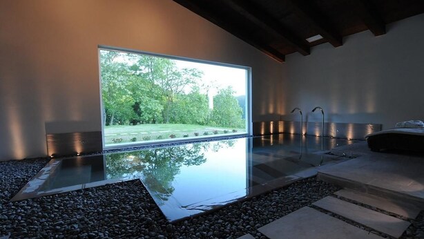 Un interior moderno con un gran ventanal, una fuente de agua reflectante y un camino de piedra.