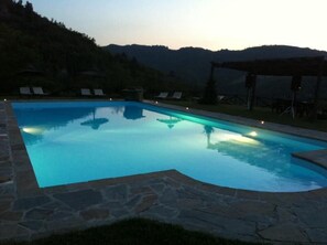 Una piscina rectangular con borde de piedra, rodeada de sillones de descanso y una pérgola.