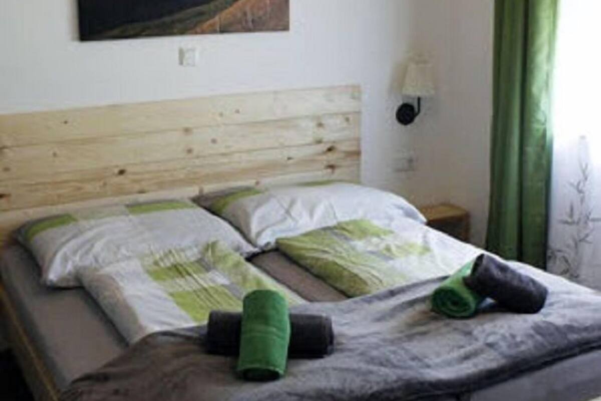 A bedroom with a wooden bed frame, a green headboard, a painting of mountains on the wall, and a bedside lamp.