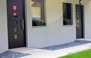 A modern building with a dark-colored door, two windows, and a small garden area with gravel and grass. - Nature Fun Apartments (Hermagor-Pressegger See)