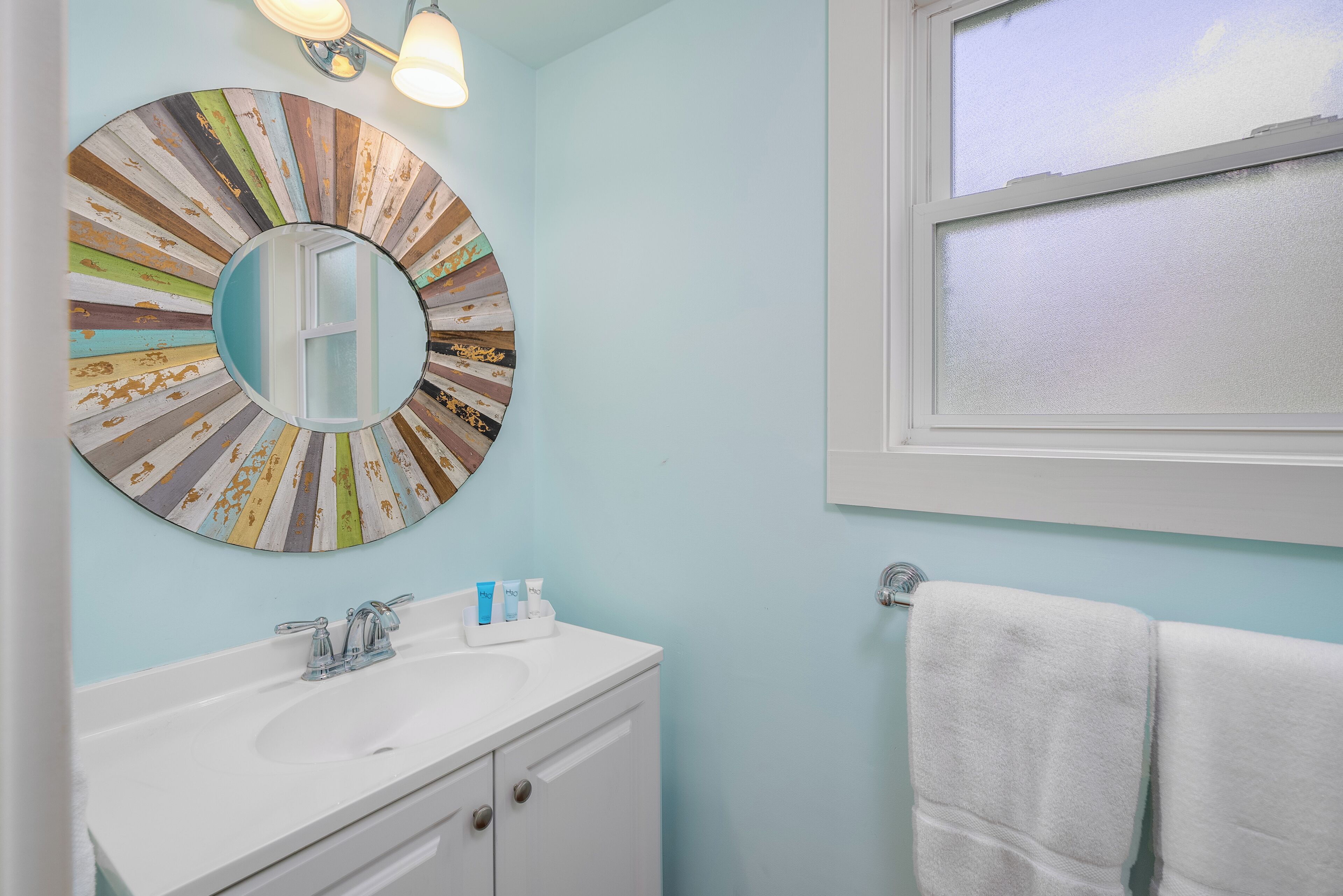 A bathroom with a round mirror, white sink, and a window with a view of the sky.