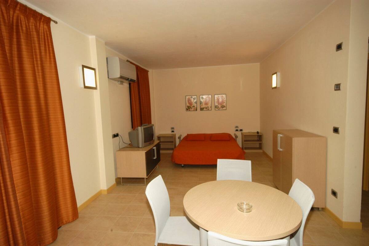 A hotel room with a bed, a TV, a desk, a chair, a table, and a curtain.