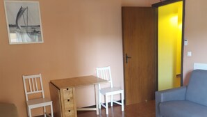 Una stanza con un tavolo di legno, due sedie bianche, un divano blu e una porta che dà su un'altra stanza.