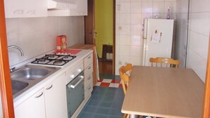 Una cucina compatta con mobili bianchi, piano cottura a gas, lavello e frigorifero.
