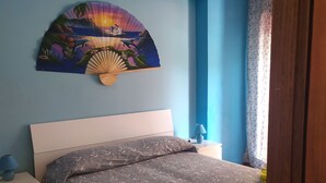 Una camera da letto con un letto, un comodino, una lampada, una ventola a soffitto e un ventilatore a parete.
