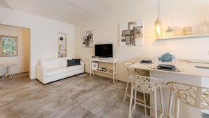 Un saló modern amb un sofà blanc, una televisió, zona de menjador amb cadires i una barra de cuina.