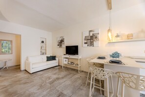 Un salon moderne avec un canapé blanc, un téléviseur, un coin repas avec des chaises et un comptoir de cuisine.