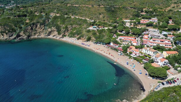 Vista aèria d'una zona costanera amb una platja, cases i mar blau cristal·lí.