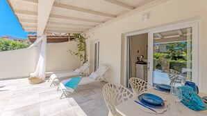 Un porxo cobert amb una taula preparada per dinar, seients de relaxació i una vista a través d'una porta de vidre.