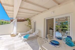 Eine überdachte Terrasse mit Esstisch, Lounge-Stühlen und Blick durch eine Glastür.