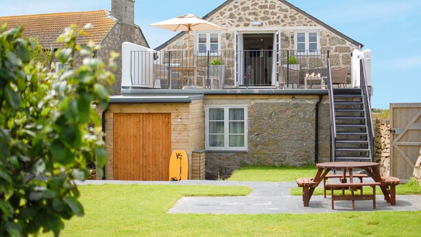 A stone house with a wooden deck, a covered patio, and a picnic table. - The Saddle and Stable Rooms (Penzance)
