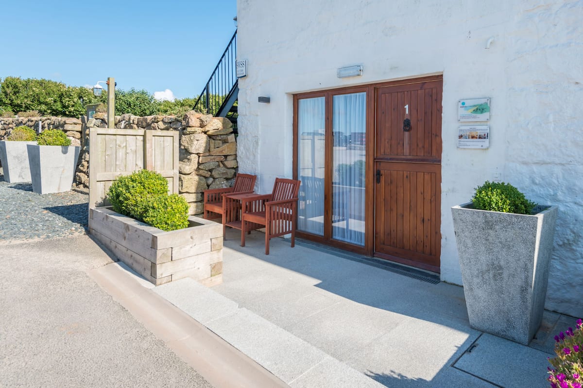 A building with a stone wall, wooden door, and a small patio with a table and chairs.