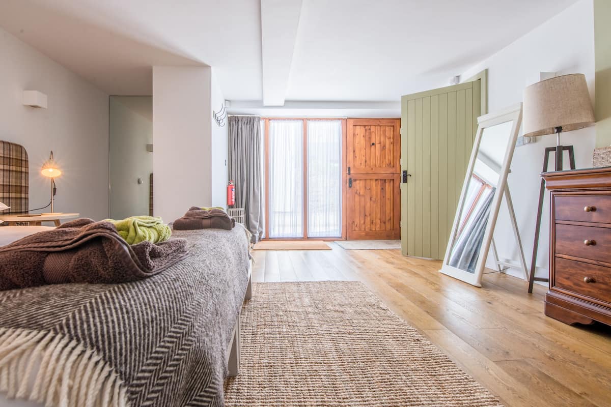 A bedroom with a bed, bedside table, lamp, and a view of a wooden door and window.