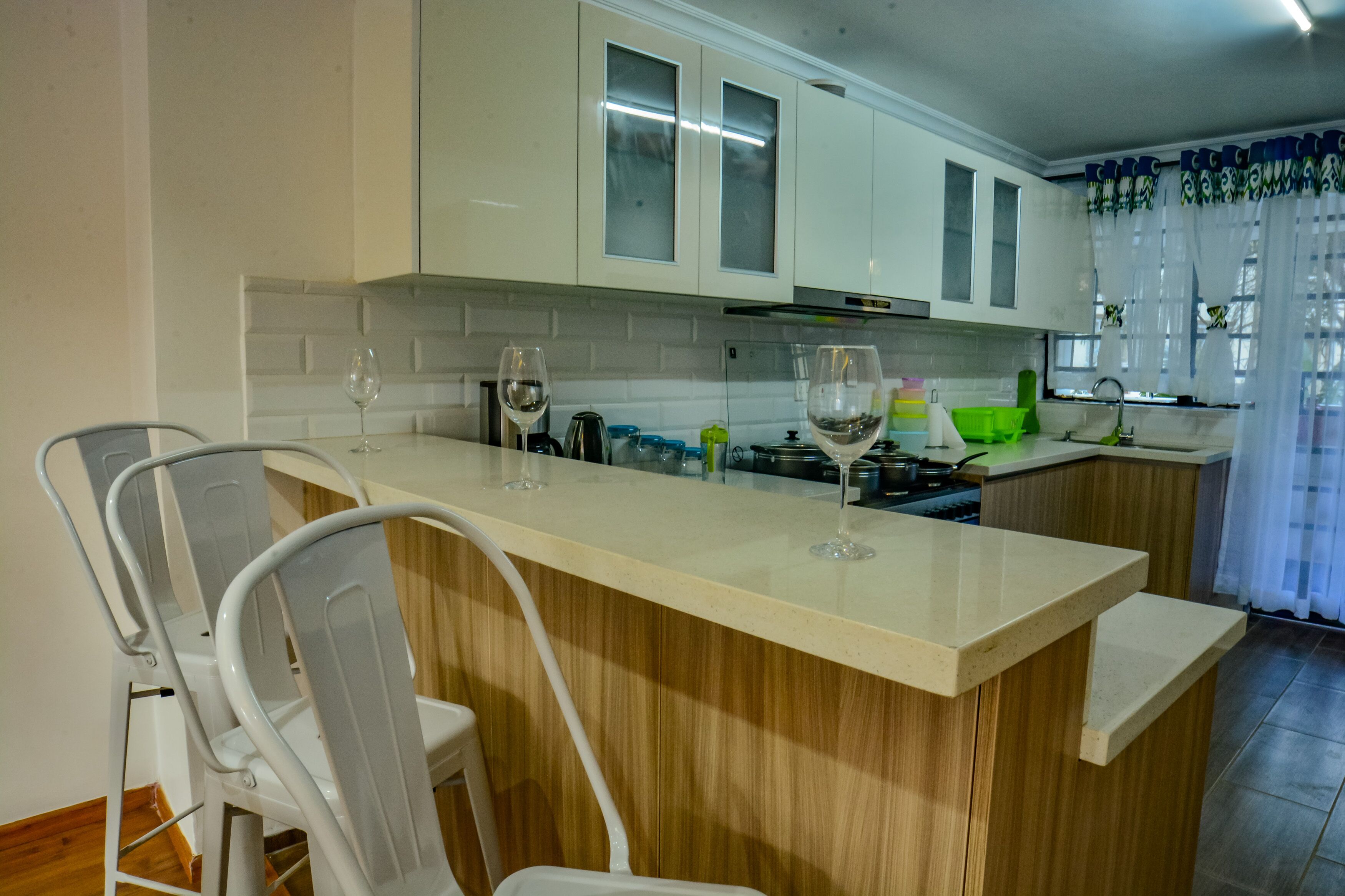 A kitchen with white cabinets, a wooden island, and two white chairs.