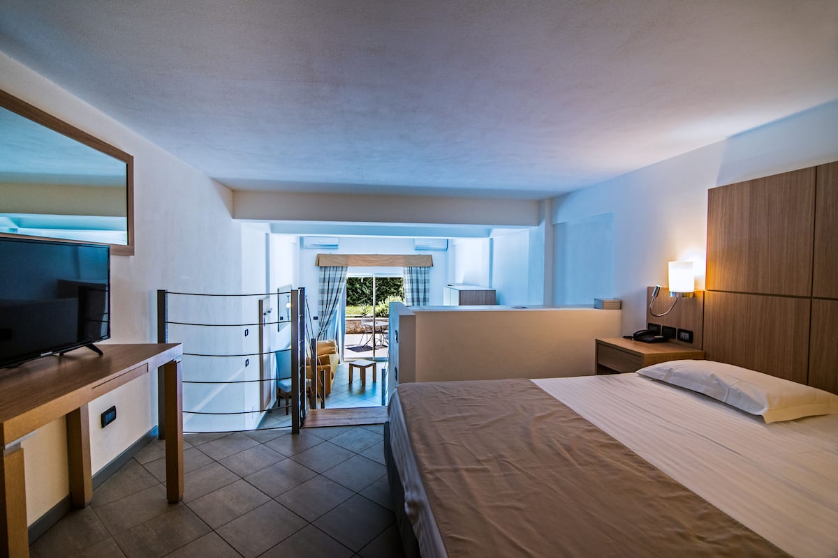 Quarto de hotel moderno com cama, escrivaninha, televisão, guarda-roupa e varanda com vista.