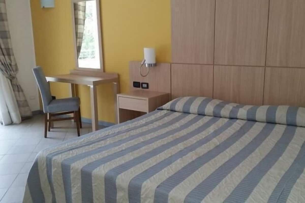 Quarto de hotel com cama, escrivaninha, cadeira e janela.