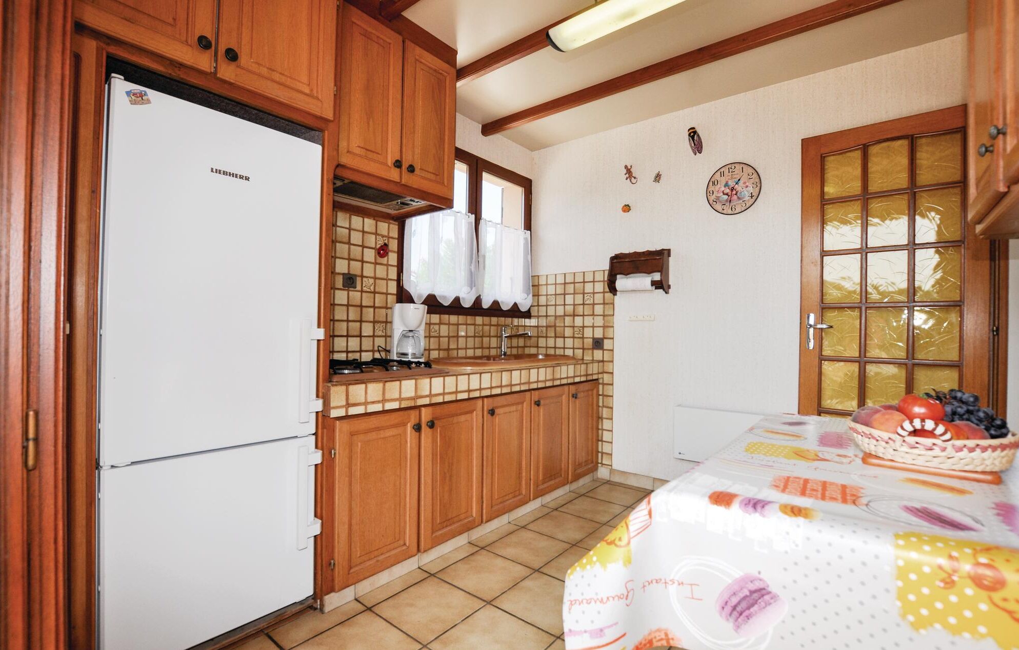 A kitchen with wooden cabinets, a white refrigerator, a tiled backsplash, a coffee maker, and a fruit basket on the table.