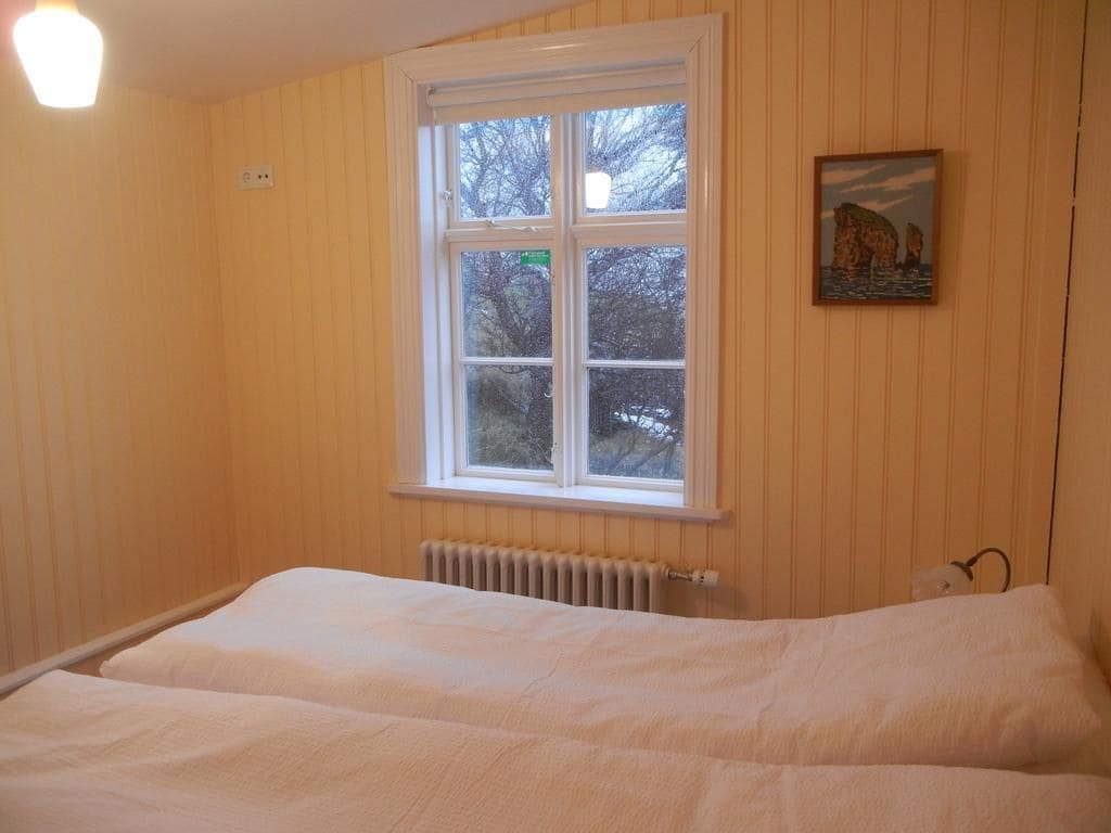 A bedroom with a large window, a radiator, and a painting on the wall.