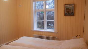 A bedroom with a large window, a radiator, and a painting on the wall.