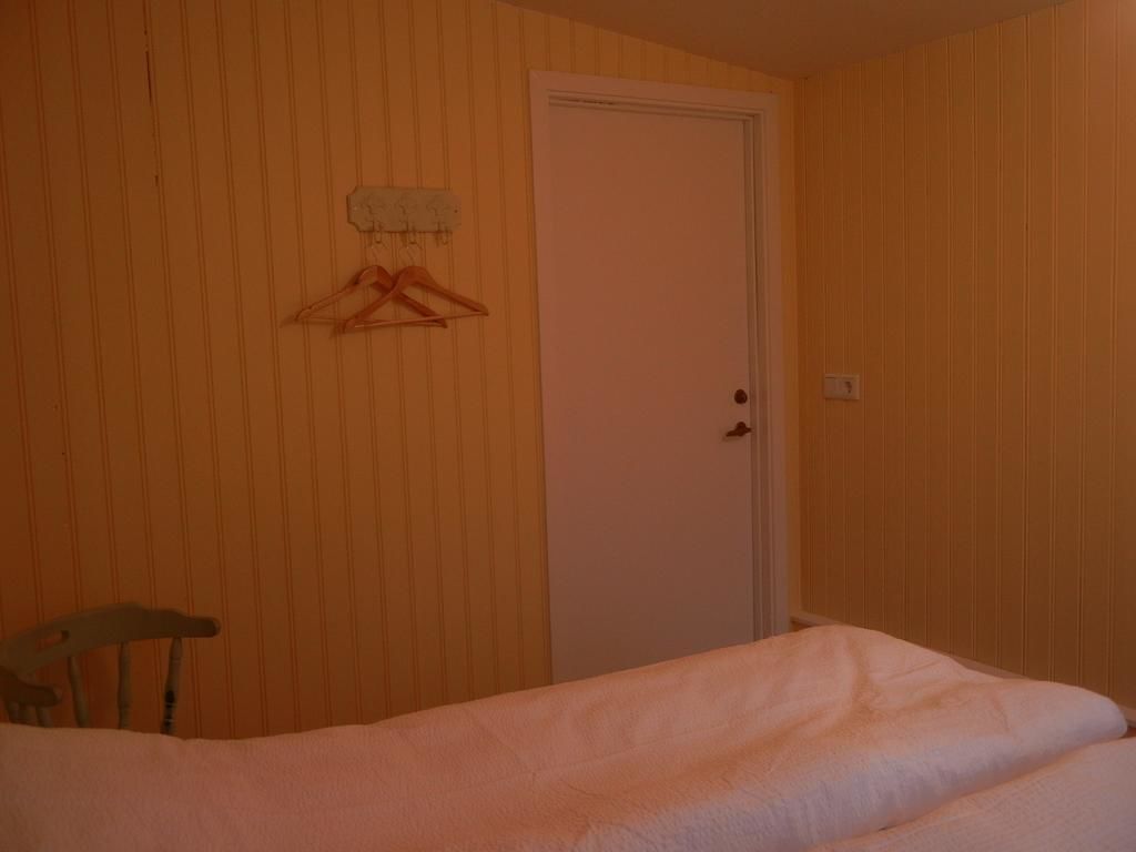 Una stanza con un letto, una sedia di legno, una porta bianca e un appendiabiti con una gruccia.