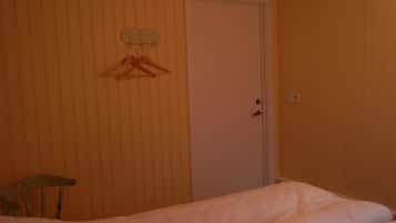 Una stanza con un letto, una sedia di legno, una porta bianca e un appendiabiti con una gruccia.