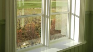Ein Fenster mit Blick auf ein grünes Feld und eine entfernte Hügelkette.