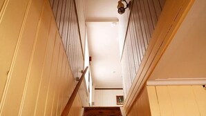 Eine Holztreppe mit weißen Wänden und einer Lampe am oberen Ende.