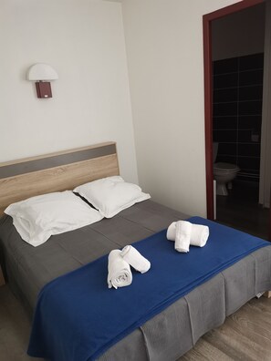Una camera d'hotel con un letto, cuscini bianchi, una coperta blu e due asciugamani arrotolati sul letto.