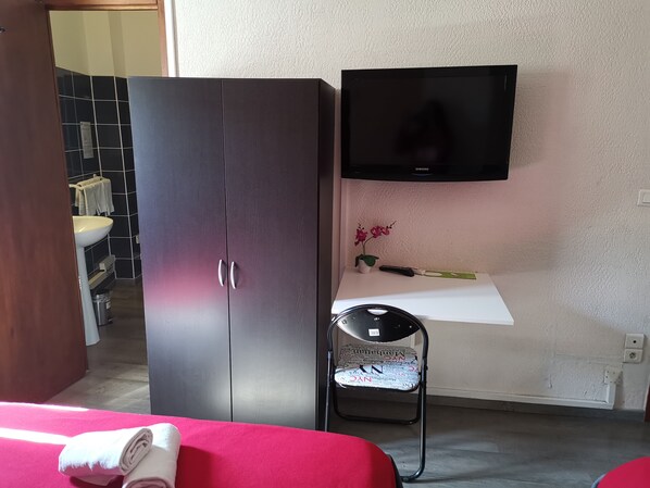A room with a bed, a wardrobe, a television, a small table with a vase, and a chair. - Hotel Le Cheval Blanc (Uchaud)