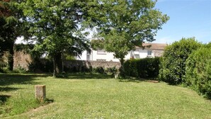 Un espace extérieur verdoyant, avec un mur de pierre, un arbre et un bâtiment en arrière-plan.