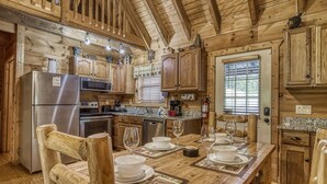 Cocina rústica de madera con una mesa de comedor para cuatro personas, sillas de madera y un refrigerador.