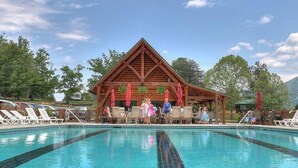A pool area with lounge chairs and a wooden building with a triangular roof. - Two Bedroom Cabin-Theater Room & Gameroom! Outdoor Pool Access in Wears Valley close to Pigeon Forge (Sevierville)