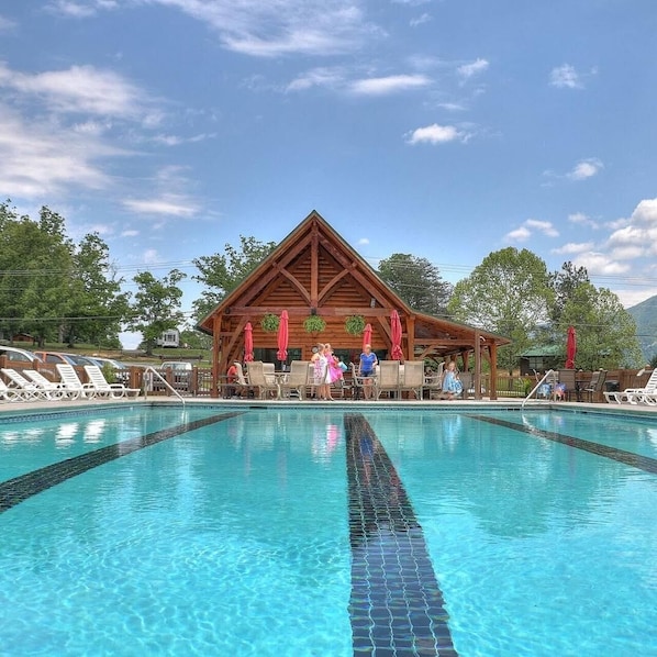 A swimming pool with lounge chairs and a wooden building in the background.