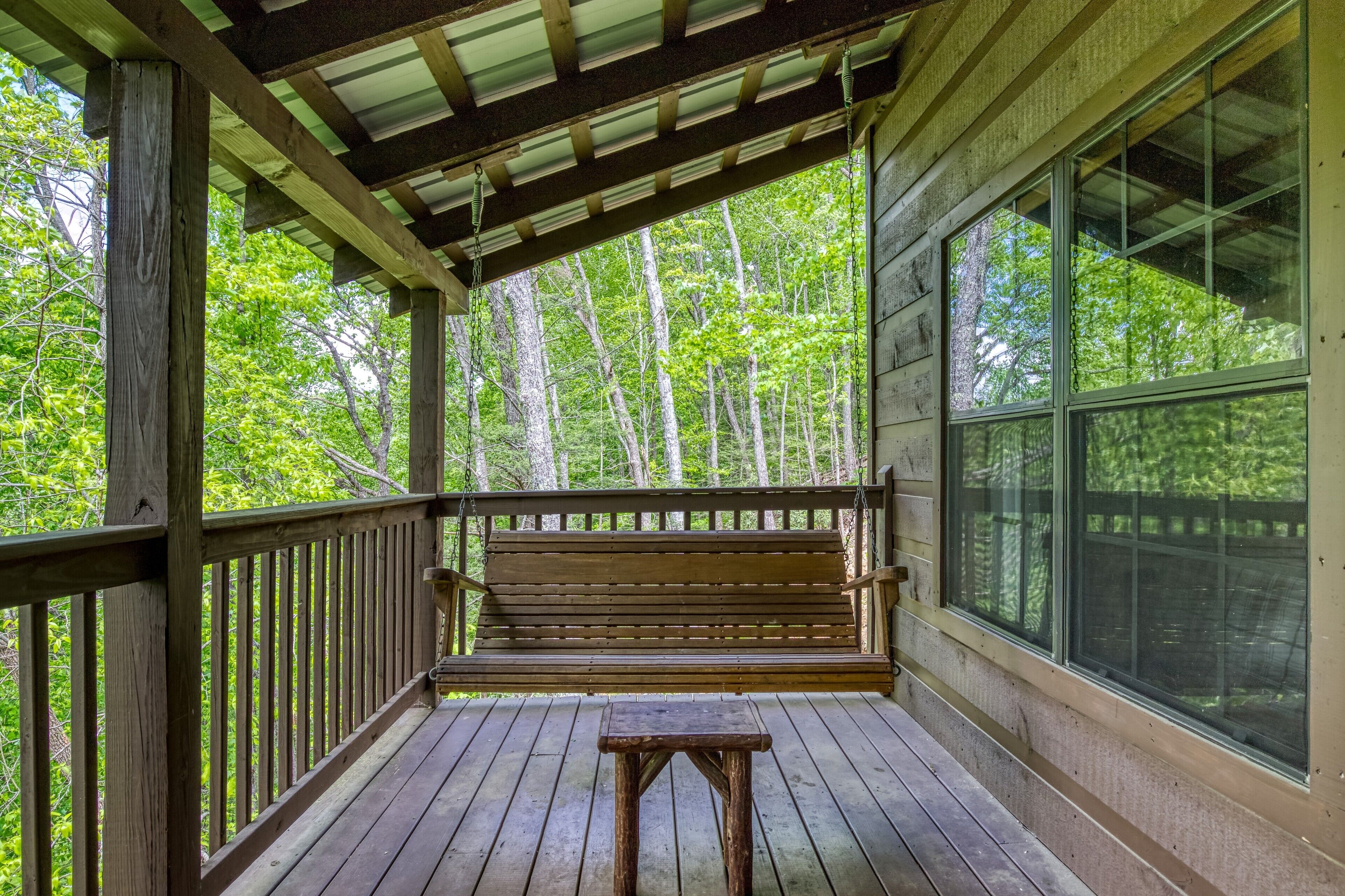 A wooden deck with a bench and a table, surrounded by trees.