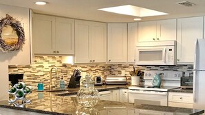 A modern kitchen with white cabinets, a granite countertop, and stainless steel appliances.