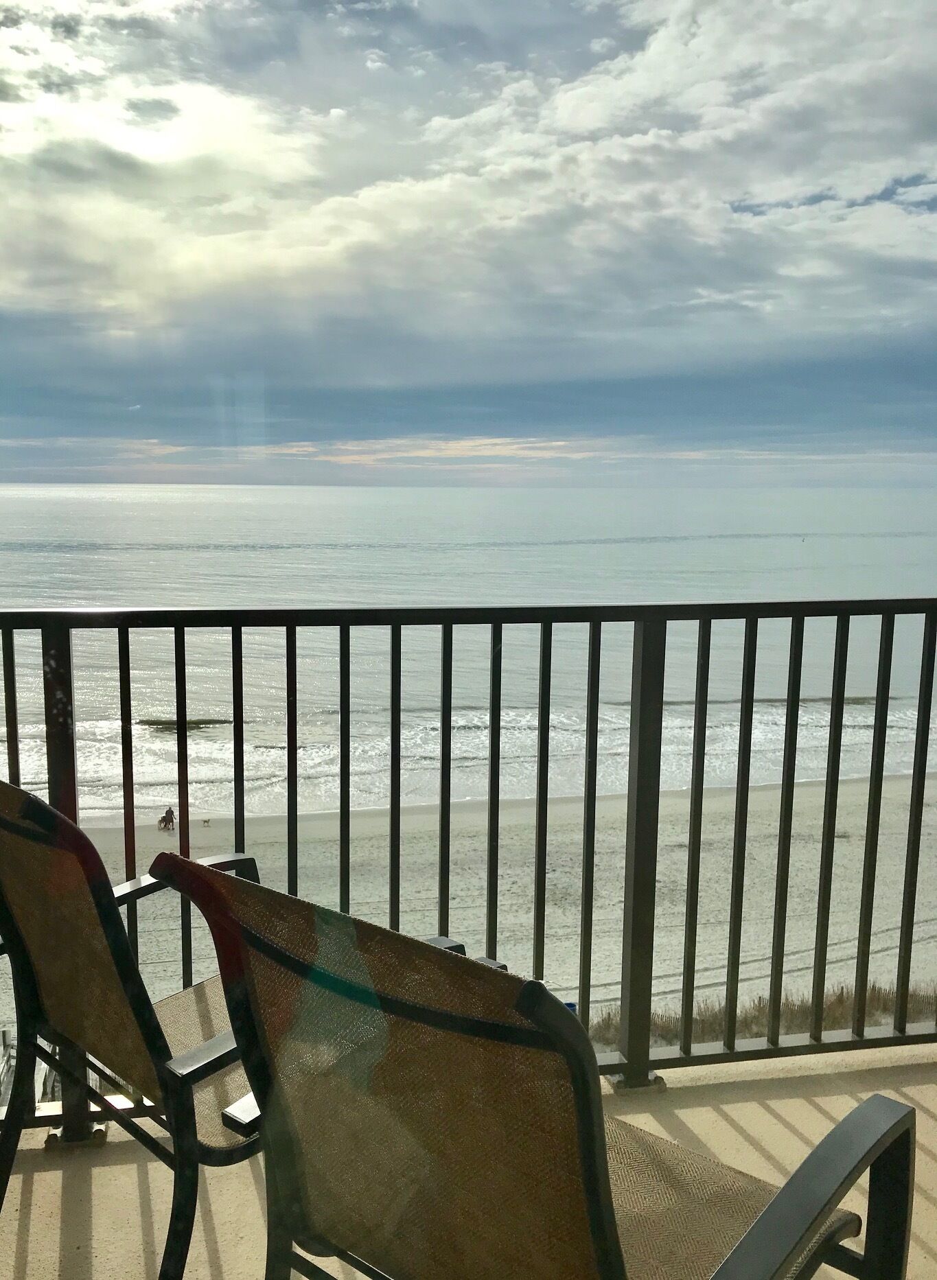 A balcony with a view of the ocean and beach. There are two chairs and a table.