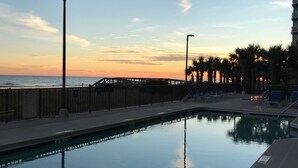 A swimming pool with a view of the ocean at sunset, a wooden deck, and palm trees.
