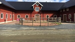 A red barn with a black roof, a fenced riding area, and a gravel driveway. - Bashults Gård (Jonkoping)