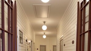 A hallway with wooden floors, white walls, and brown doors. There are two light fixtures on the ceiling, a small table with a lamp, and a rug on the floor. - Bashults Gård (Jonkoping)