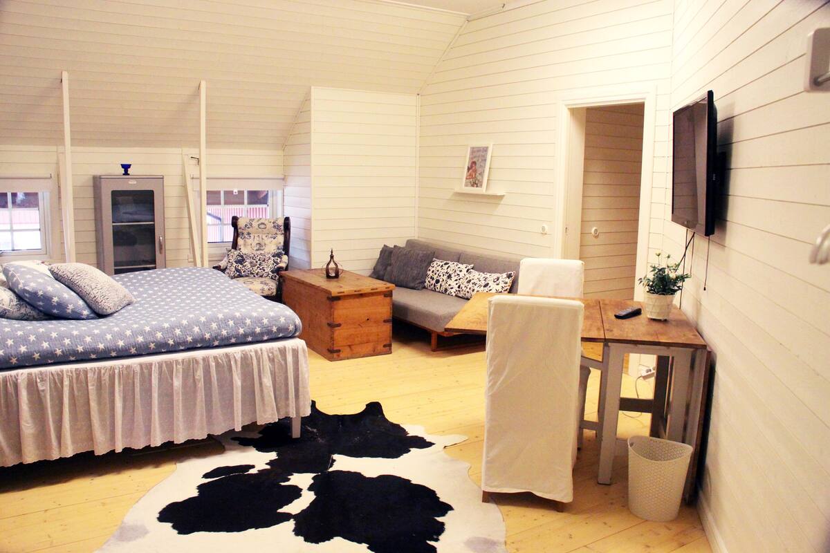 A bedroom with a bed, a sofa, a wooden chest, a television, and a window.