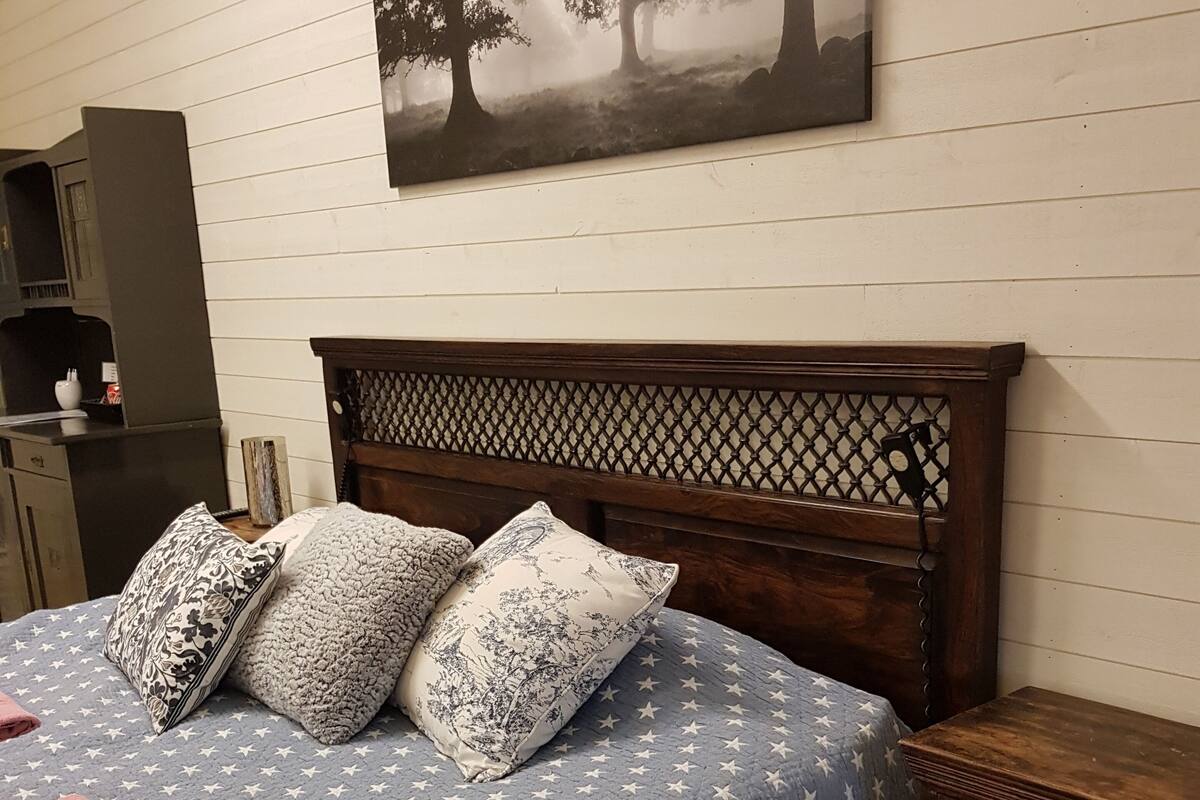 A bedroom with a bed, pillows, a nightstand, a wooden headboard, a wall-mounted picture, and a small cabinet.