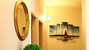 A hallway with a large mirror, a potted plant, and a painting of a lighthouse. - Guleryuz Otel (Ankara)