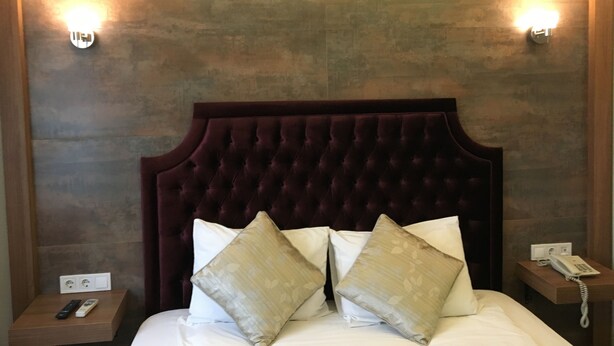 A hotel room with a tufted headboard, two bedside lamps, a bedside phone, and a nightstand with a remote control. - Guleryuz Otel (Ankara)