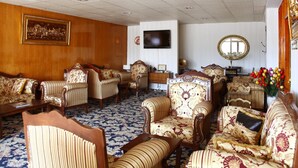 A spacious living room with a patterned carpet, wooden paneling, a flat-screen TV, and a large mirror. - Guleryuz Otel (Ankara)