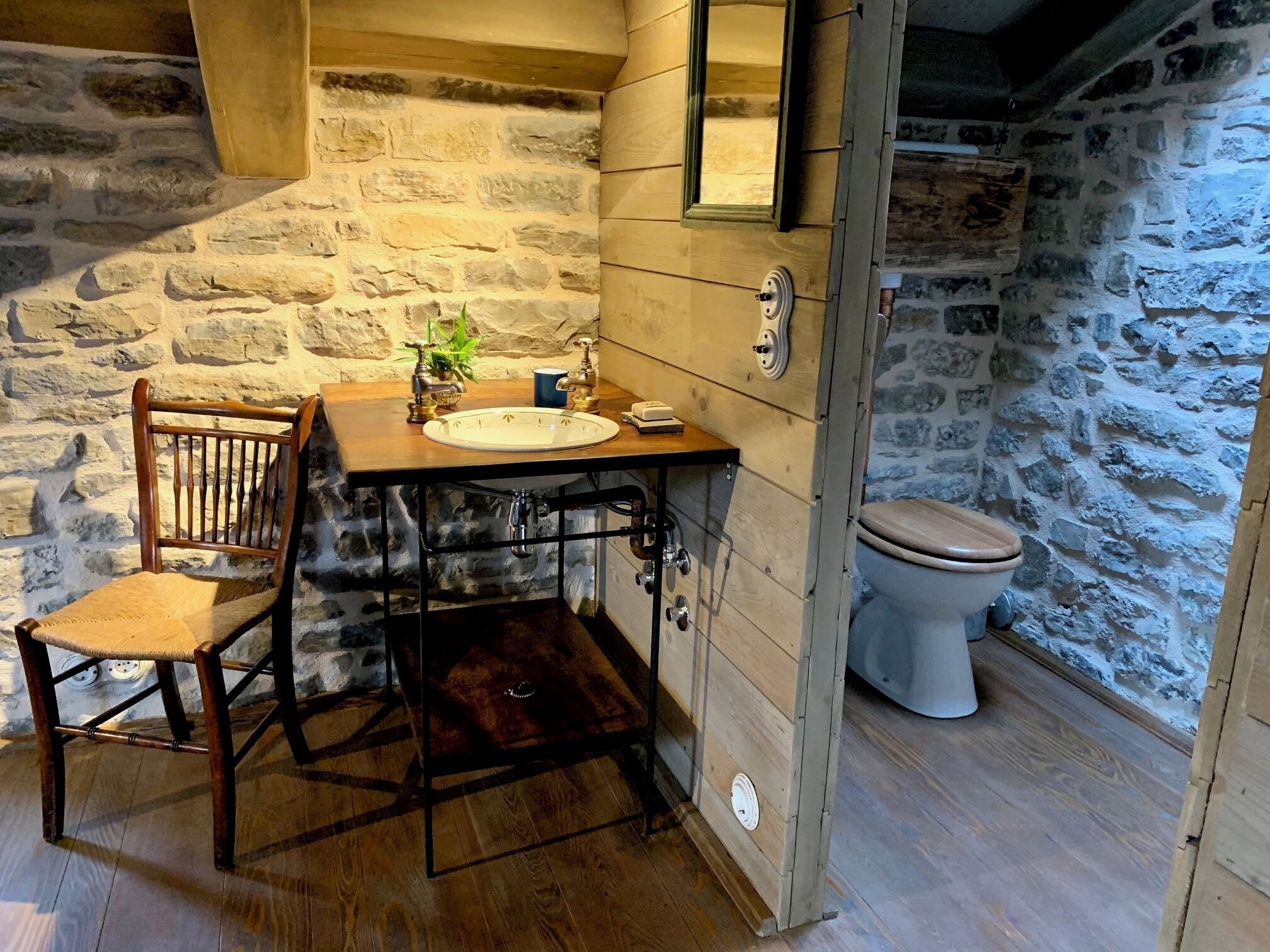 A rustic bathroom with a wooden vanity, a toilet, and a stone wall.
