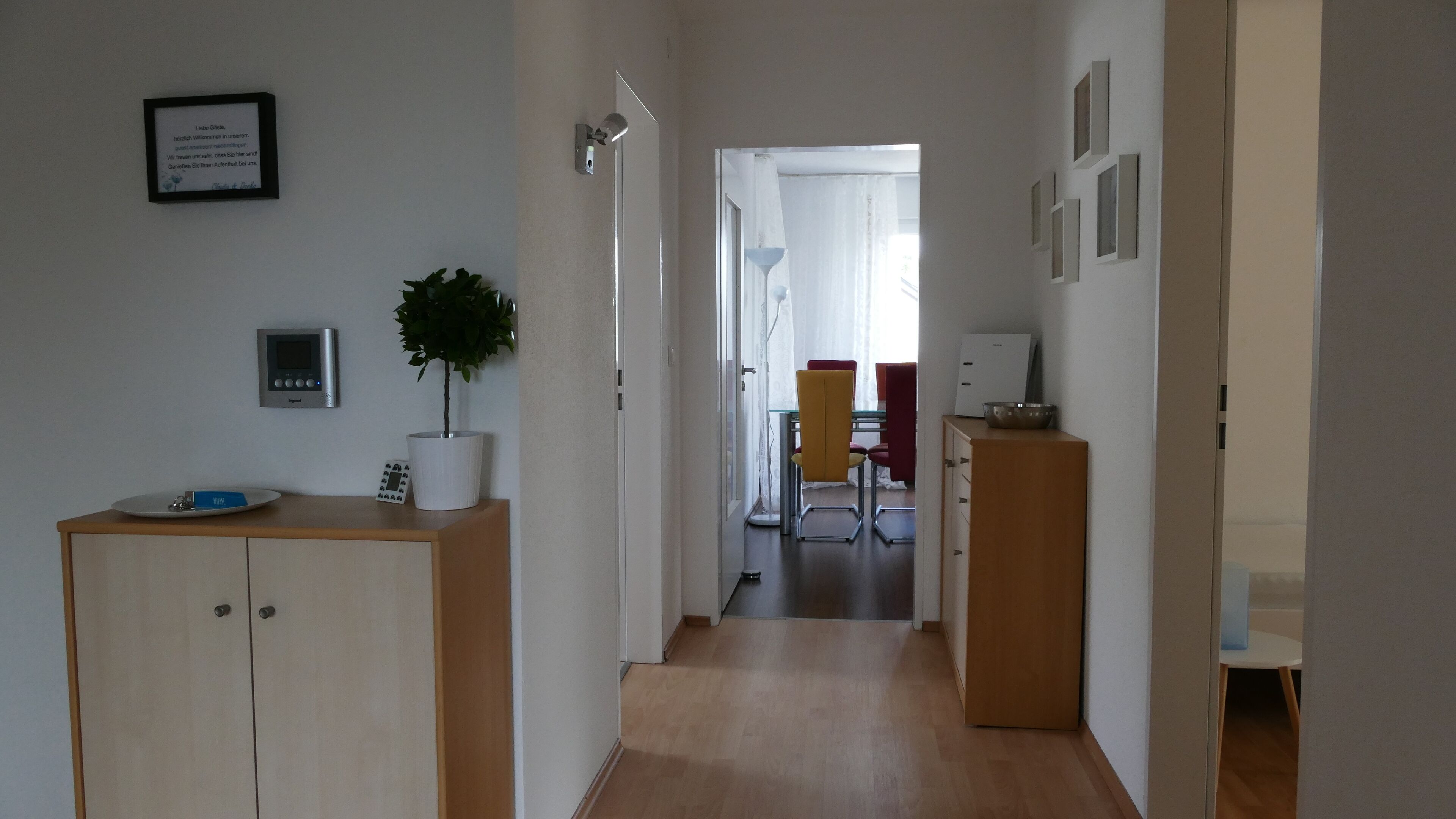Ein Flur mit einem Holzschrank, einem Blumentopf, einem Willkommensschild und einem Essbereich im Hintergrund.