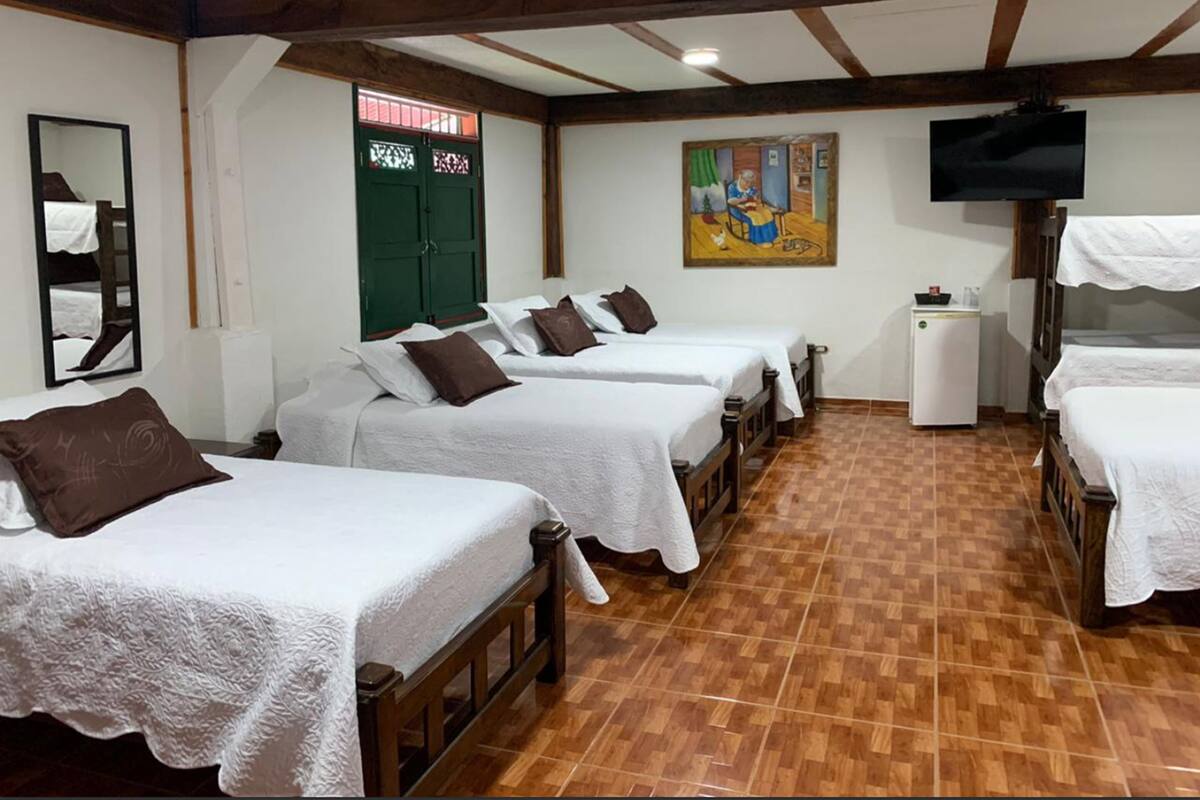 Une chambre d’hôtel avec quatre lits simples, un petit réfrigérateur, une télévision et un tableau au mur.