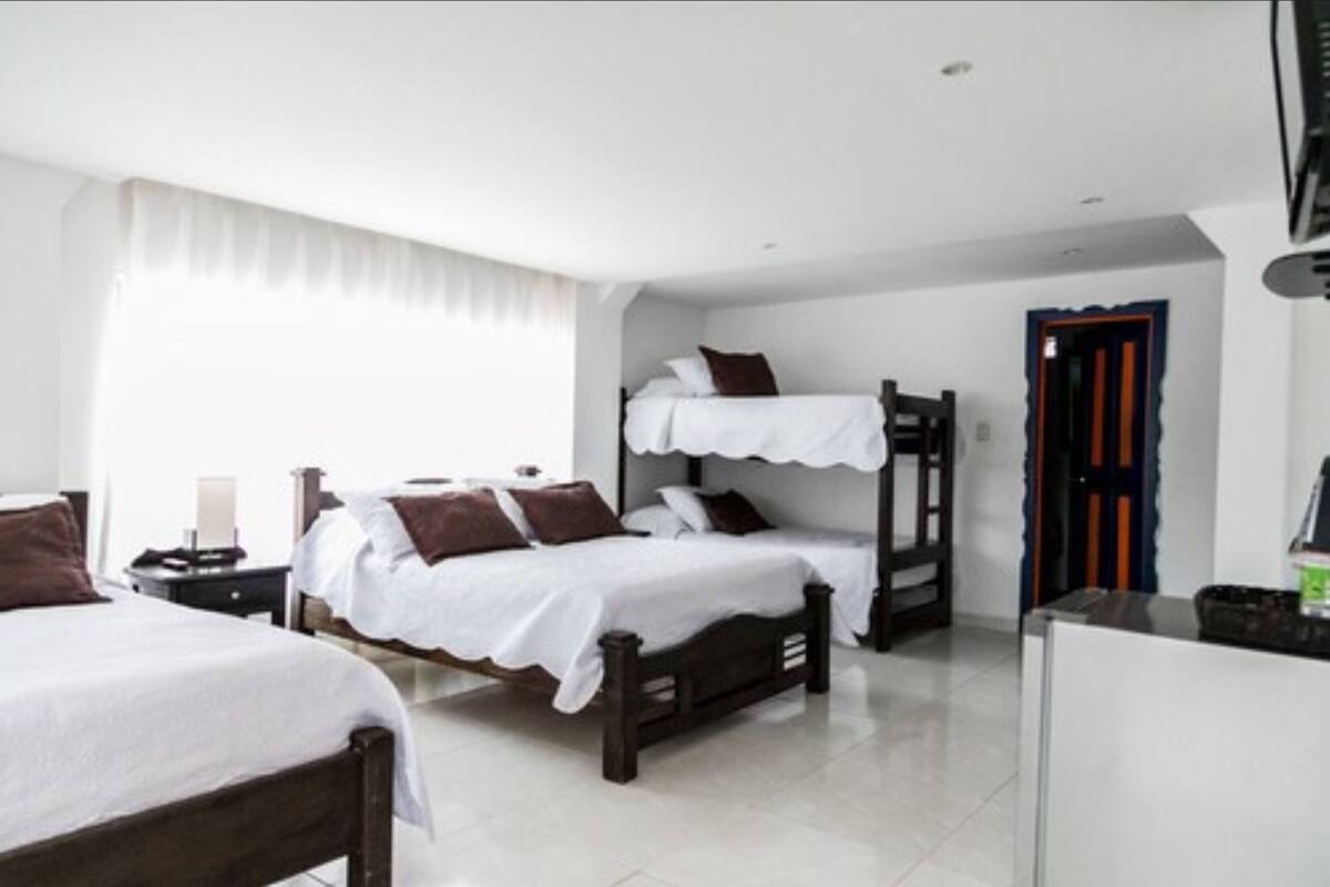 Une chambre d’hôtel avec deux lits simples et un lit superposé, des murs blancs et un sol carrelé.