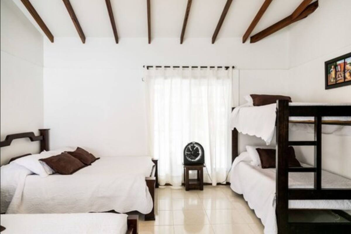 Une chambre avec un lit superposé, une table de chevet avec une horloge et une fenêtre avec des rideaux blancs.