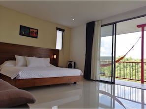 A hotel room with a large bed, a small table, a chair, a window with blinds, a wall-mounted light, and a balcony with a hammock. - Finca Hotel La Manuela (Montenegro)